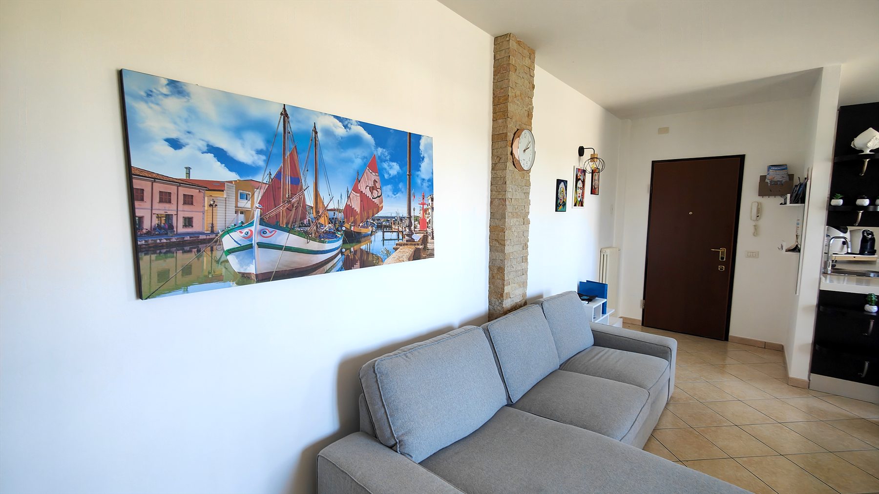 Il soggiorno visto dall'ingresso: divano grigio e il quadro del porto canale di Cesenatico
